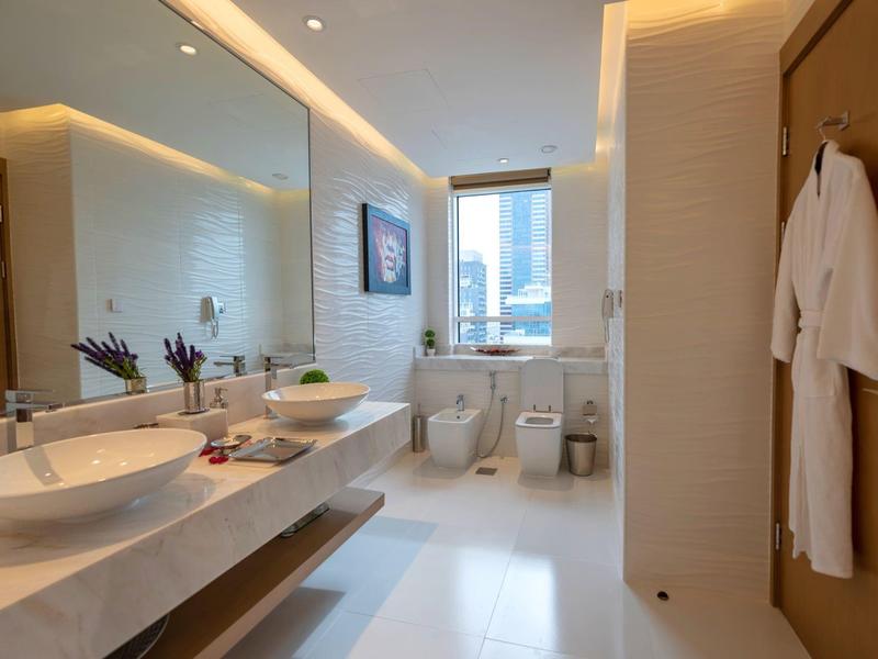 Modern hotel bathroom with double sinks, large mirror, window with city view, and white bathrobes.