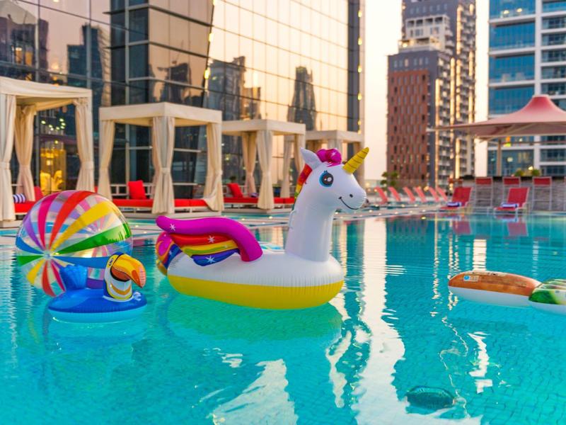 Colorful inflatable pool toys float in an urban pool with skyscrapers in the background.