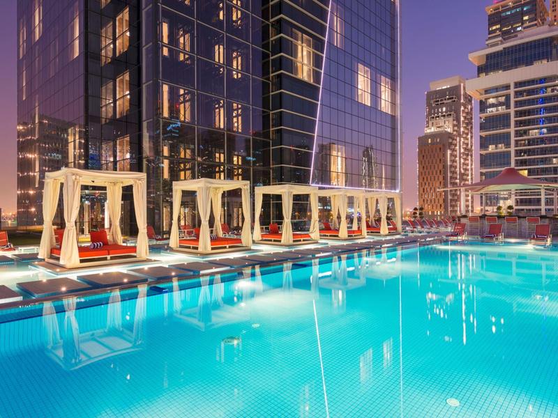 Modern rooftop pool with cabanas and city view at dusk.