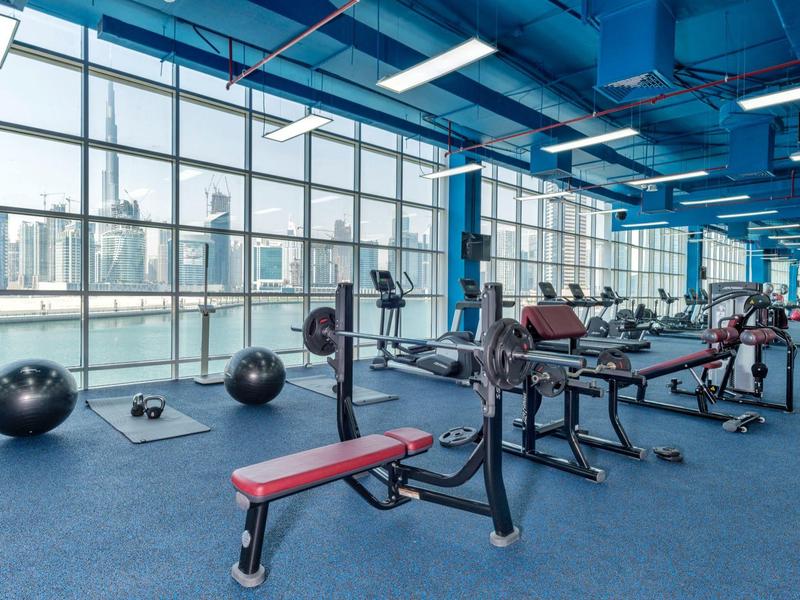 Gym with weights and benches by large windows overlooking cityscape