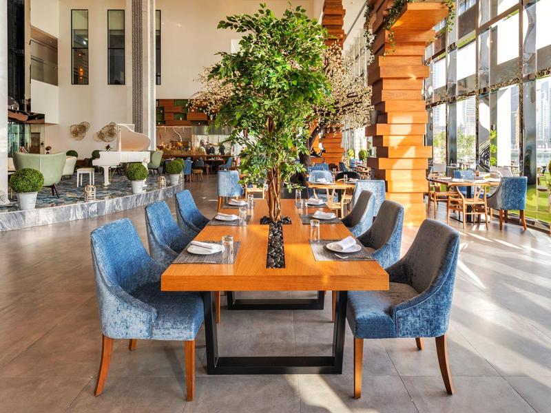 Bright dining room with long wooden table, blue chairs, and large windows.