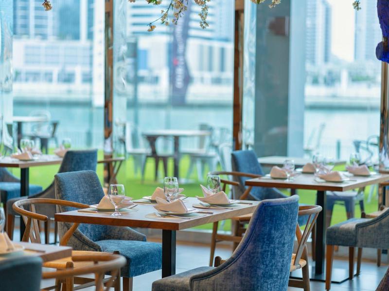 Modern restaurant with wooden furniture and blue upholstered chairs in daylight.