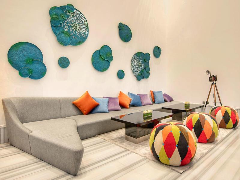 Modern living room with gray sofa, colorful cushions, and geometric poufs.