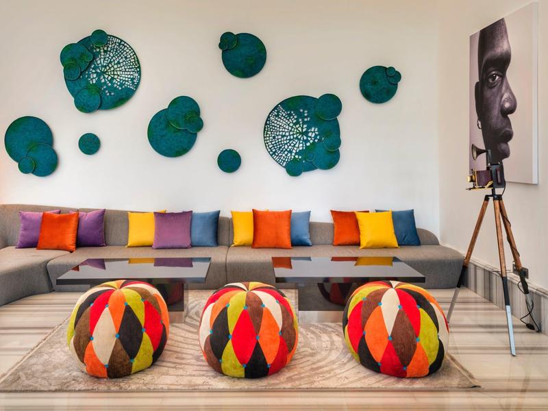 Modern seating area with gray sofa, colorful cushions, patterned poufs, and a portrait lamp.