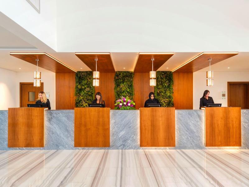 Modern hotel lobby with wooden and marble reception desk, illuminated by hanging lamps.