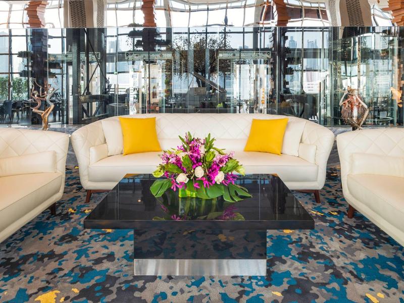 Elegant hotel lounge with white sofas, colorful carpet, and central floral arrangement on black table.