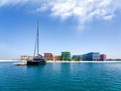 Bunte Hotels am Ufer mit blauem Meer und Segelboot im Vordergrund unter bewölktem Himmel.