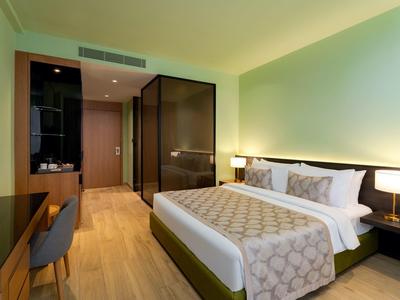 Modernes Hotelzimmer mit großem Bett, Holzfußboden, Schreibtisch und Glaswand zum Badezimmer.