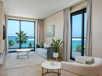 Helles Wohnzimmer mit großen Fenstern, Meerblick, Sofa, zwei Tischen und grünen Pflanzen.