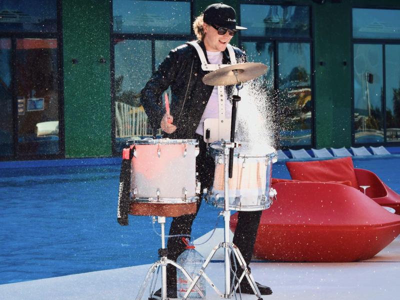 Person plays drums near pool area, splashing snow or water.