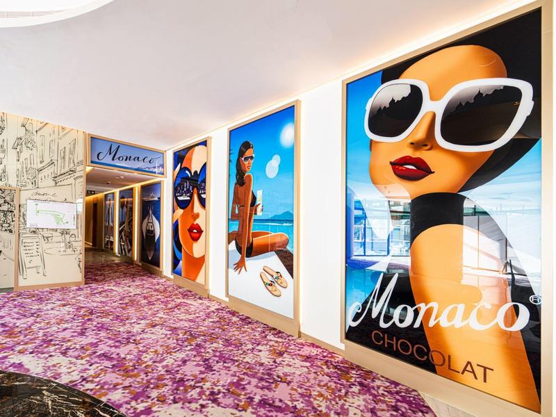 Hallway with carpet and large colorful Monaco advertisement posters on the wall.
