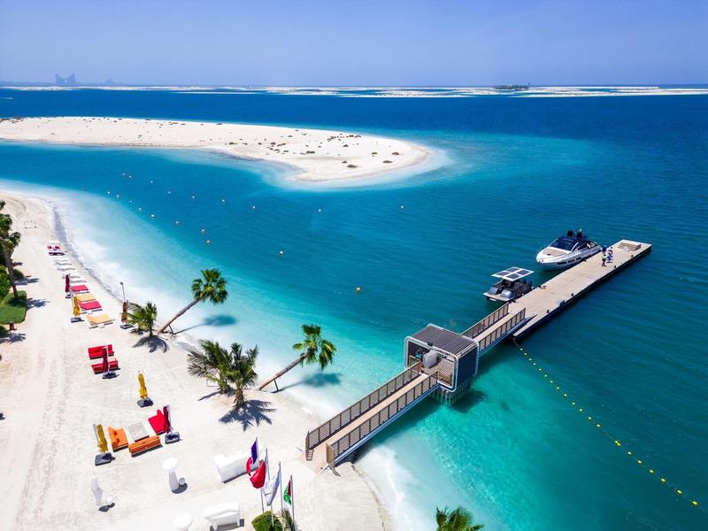 Beach with white sandbanks, turquoise water, and a pier in a tropical vacation spot.