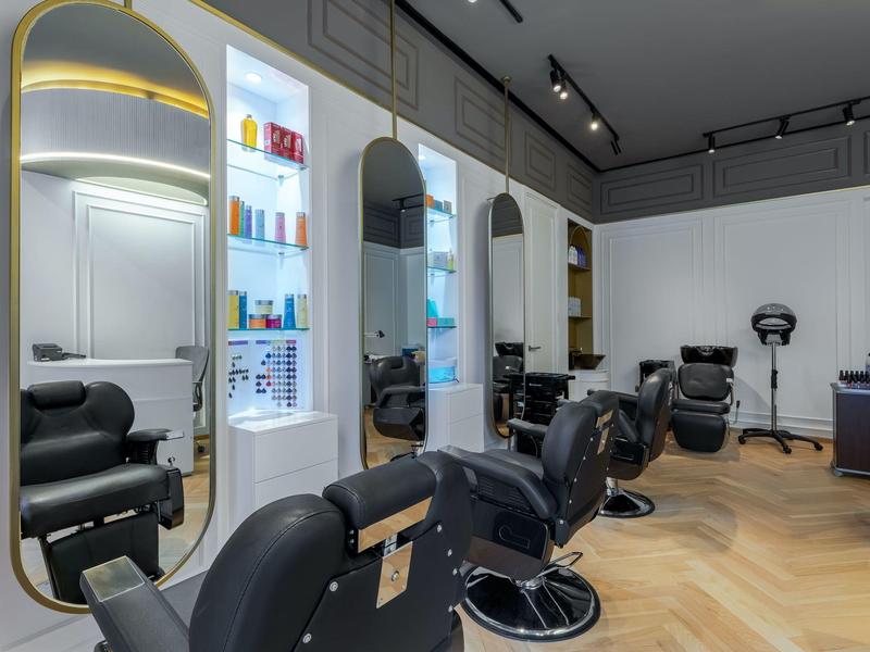 Modern hair salon with black chairs in front of illuminated mirrors and wooden floor.