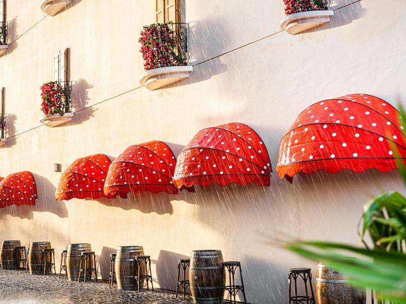 Red umbrellas and chairs on a terrace with flower boxes on the wall.