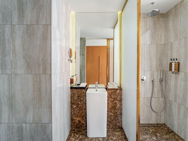Modern hotel bathroom with gray tiles, walk-in shower, and marble sink.
