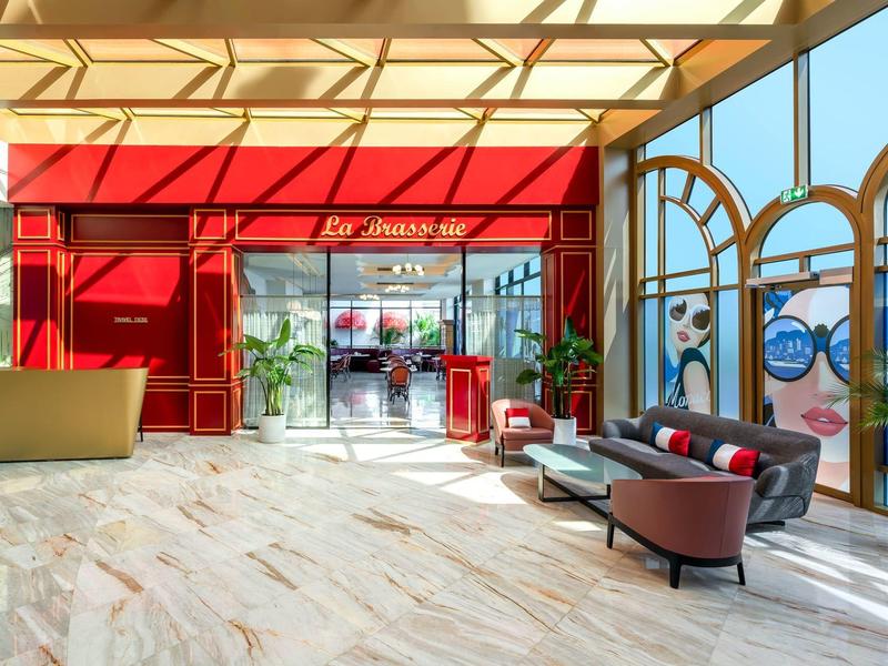 Bright hotel lounge area with large windows, sofas, and red wall decor.