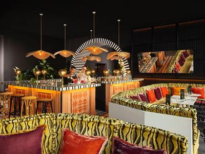 Modernes Restaurant mit farbenfrohen Sitzkissen, Holztheke, runder Bar und warmer Beleuchtung.