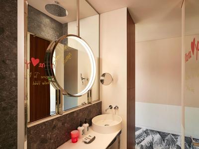 Modernes Badezimmer mit rundem beleuchtetem Spiegel, weißem Waschbecken und roter Dekoration.