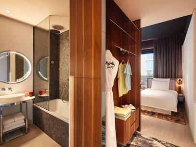 Modernes Hotelzimmer mit Bad, freistehender Badewanne und angrenzendem Schlafzimmer mit Doppelbett.