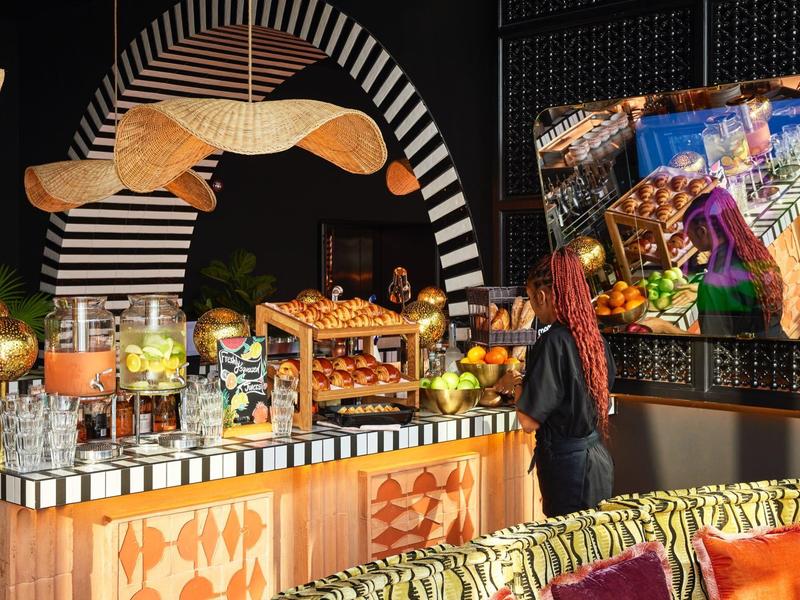 Colorfully decorated buffet with fresh pastries and a woman wearing a colorful scarf in a hotel.