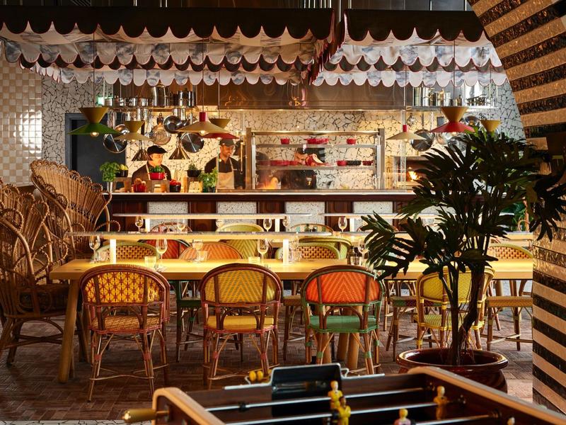 Cozy hotel lobby with bar, colorful chairs, and plants in warm lighting.