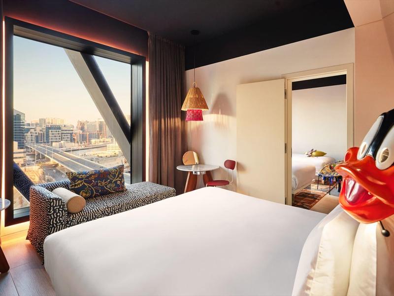 Modern hotel room with large window, city view, and cozy seating area.