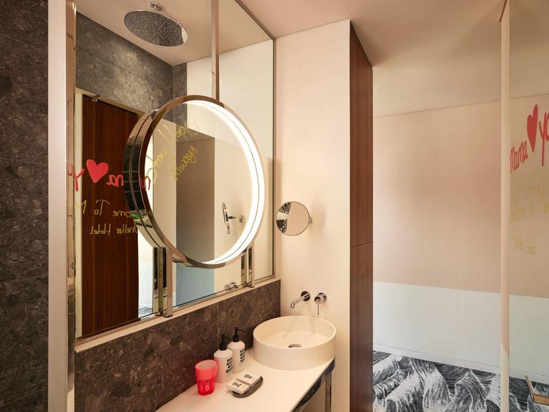Modern hotel bathroom with round illuminated mirror and stylish sink area.