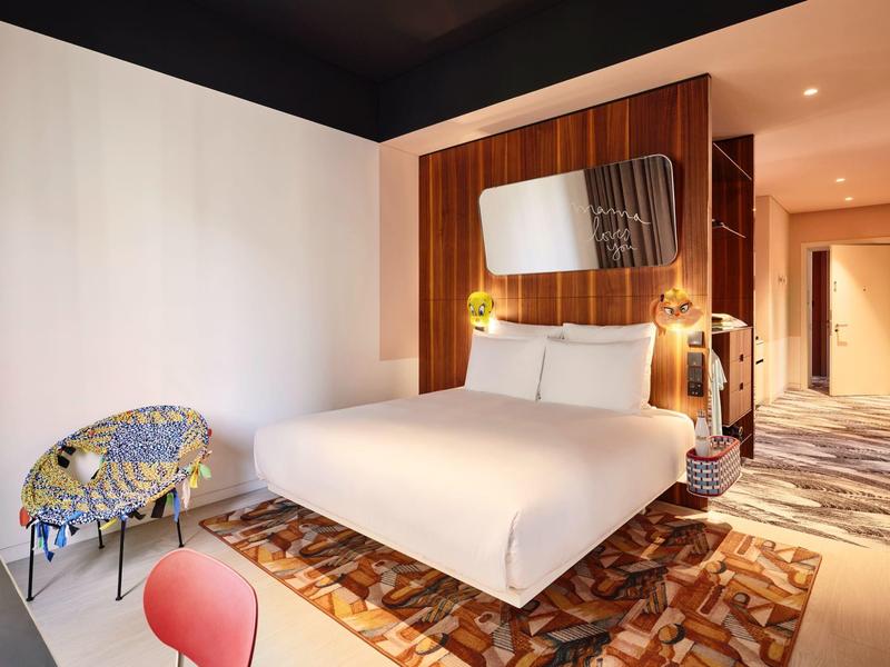 Modern hotel room with large bed, colorful carpet, and cozy chair.