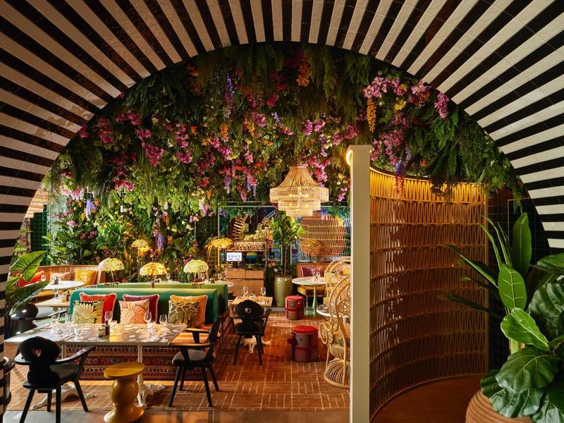 View through a round arch into a cozy café with colorful cushions and lots of plants.