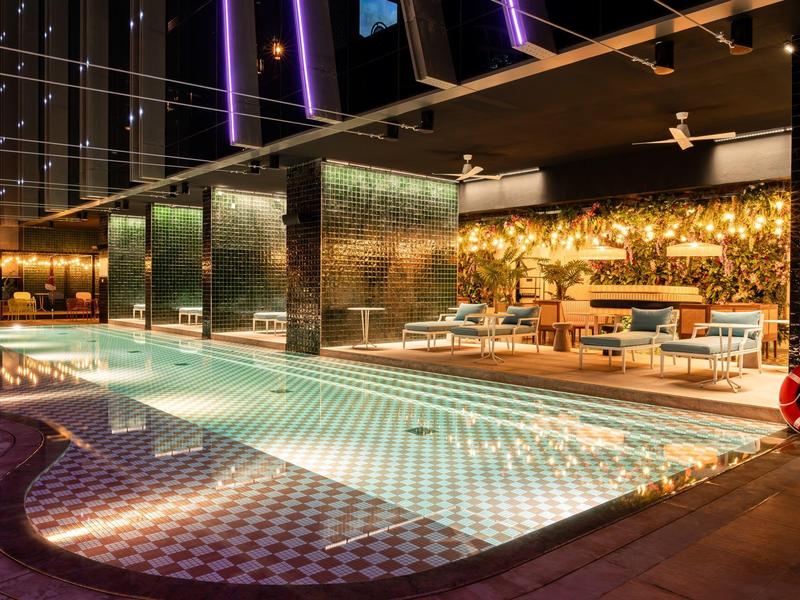 Modern illuminated outdoor pool next to stylish lounge area at night.