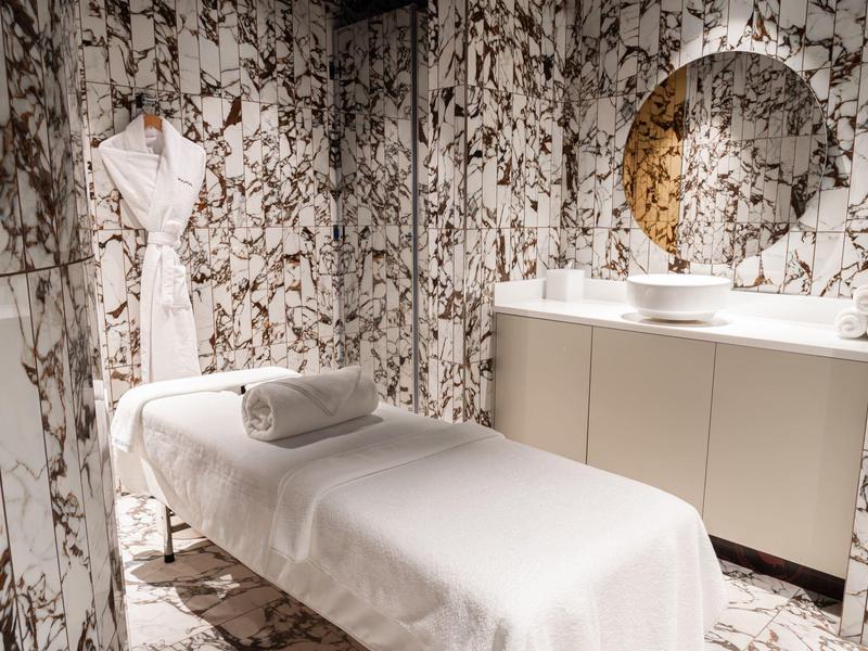 A modern spa room with massage table, towel, and marble tiles on walls and floor.
