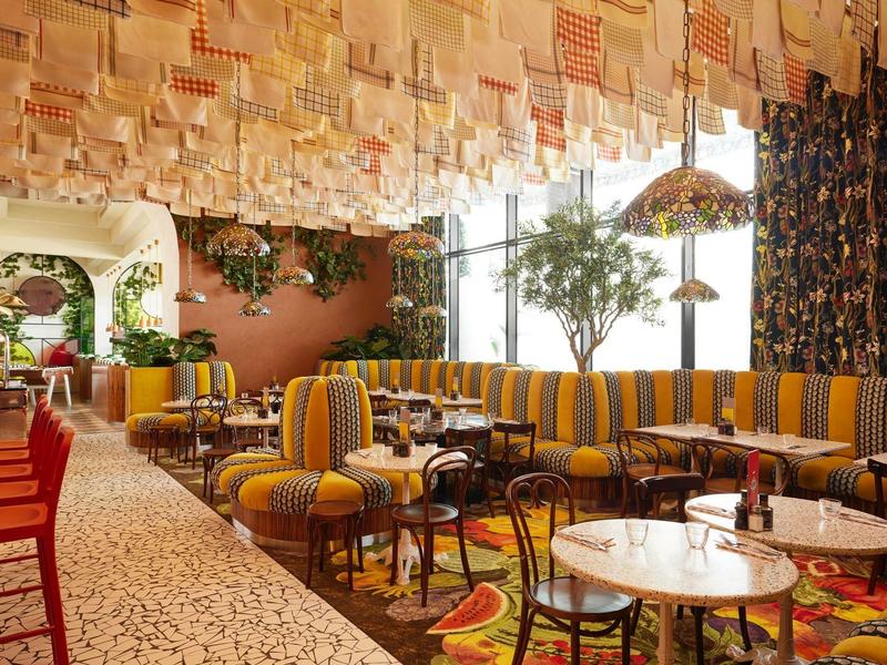 Cozy hotel bar with yellow-striped sofas, colorful chairs, and a creative ceiling design.
