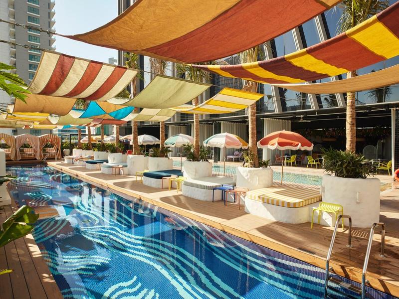 Modern hotel pool with colorful sunshades and loungers on a sunny day.