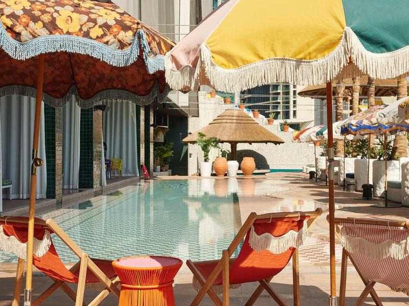 Pool area with colorful umbrellas and lounge chairs in front of a hotel building.