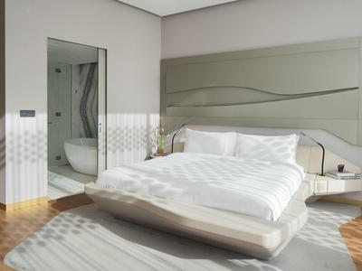 Modern hotel room with large bed, soft headboard, wooden floor, and bright natural light.