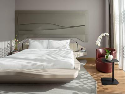 Modern hotel room with large bed, stylish headboard, armchair, and natural light from window.