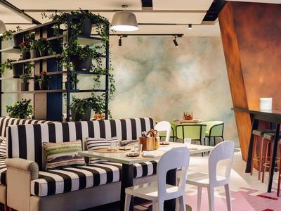 Cozy hotel lounge with striped seating, white chairs, plants, and warm lighting on patterned floor.
