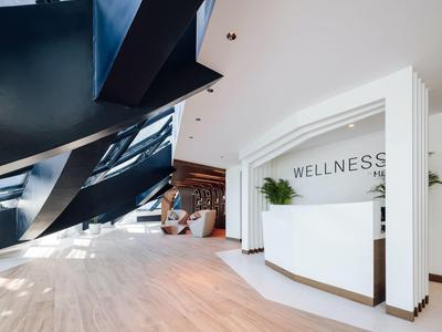 Modern wellness reception area with white design and wooden flooring under black staircase.
