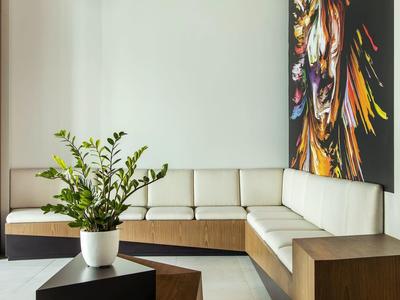 Modern hotel lounge with beige sofa, wooden tables, plant, and colorful wall art.