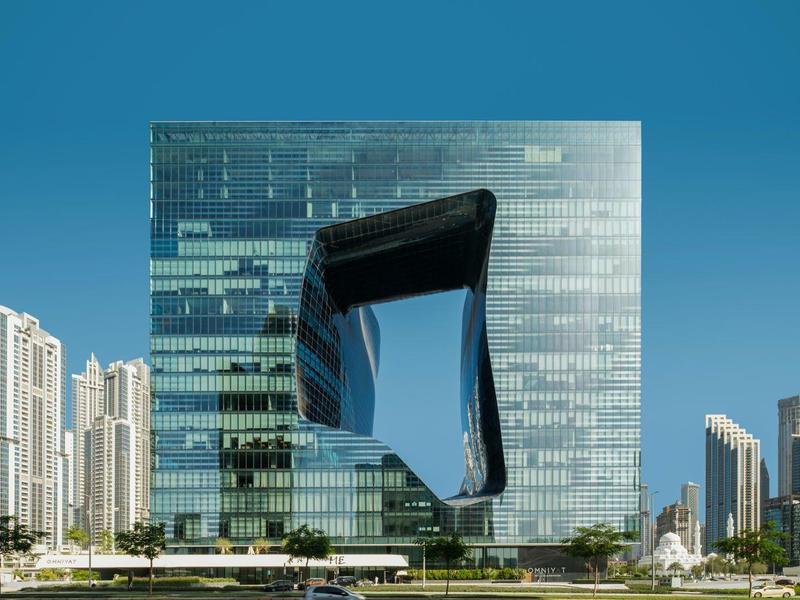 Modern cityscape with distinctive mirrored building against clear blue sky.
