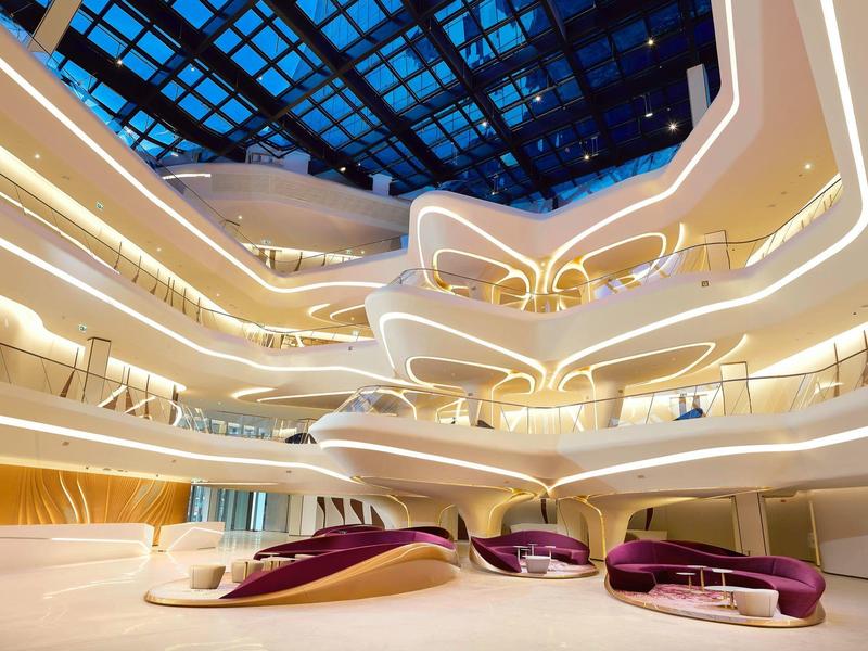 Futuristic hotel lobby with curved balconies, ambient lighting, and modern furniture under a glass ceiling.