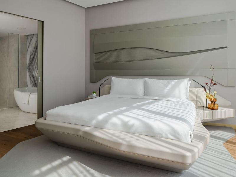 Modern hotel room with double bed, mirror, and natural light.
