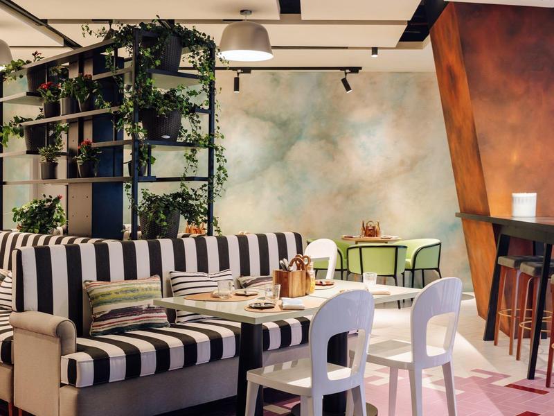 Cozy hotel lounge with striped seating, white chairs, plants, and warm lighting on patterned floor.