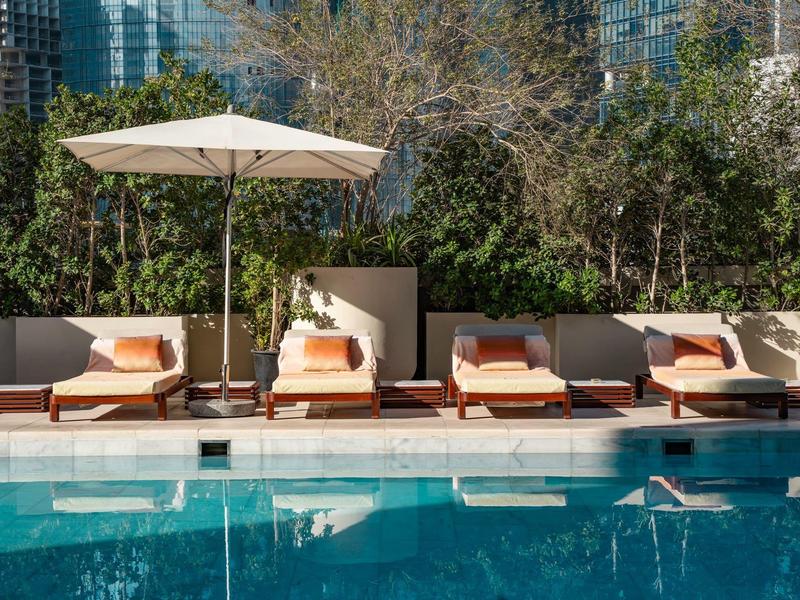 Poolside lounge chairs with cushions and umbrella by a clear blue swimming pool.