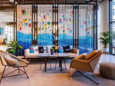 Modern lounge area with colorful hanging decor, cozy chairs, plants, and large windows.