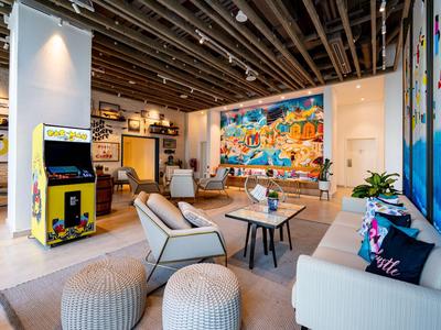 Modern eingerichteter, offener Wohnbereich mit Sofas, Stühlen, Arcade-Spielautomat und bunter Wandkunst.