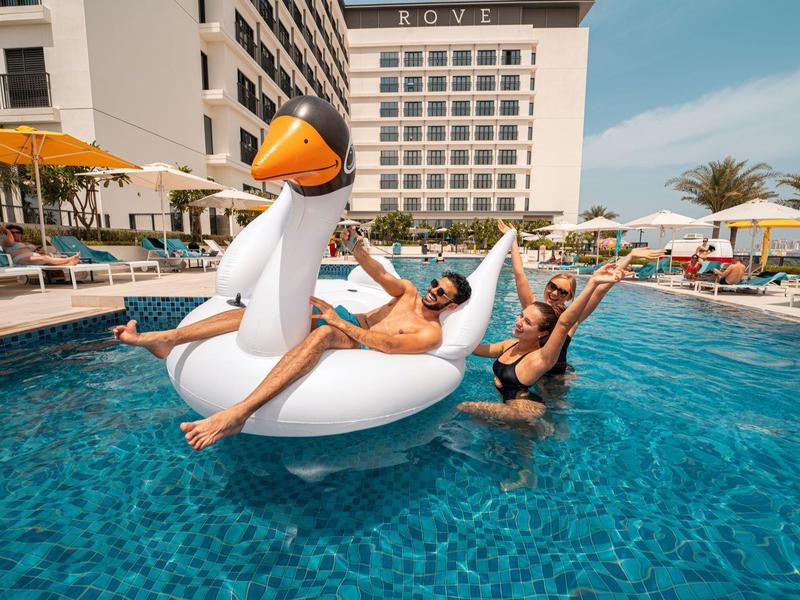 Two women enjoy a sunny day by a hotel pool, one on a large inflatable swan, the other in the water.