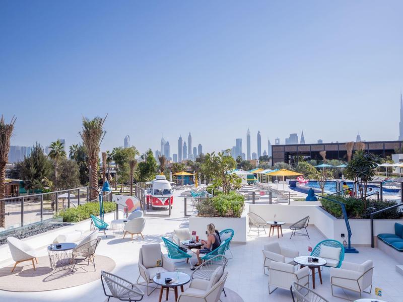 Outdoor hotel terrace with white seating and city skyline in background under clear blue sky.