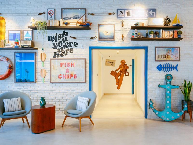 Bright hotel lobby with nautical decor, blue chairs, wooden accents, and wall art.
