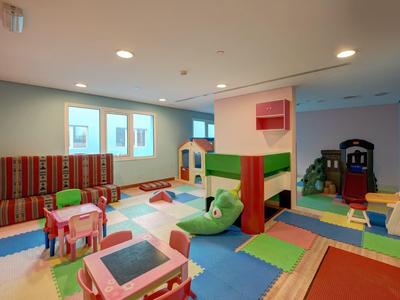 Dětská herna s barevnými podložkami, stolky, židlemi a prolézačkami v světlé místnosti.